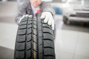 Young worker holds tire with both hands. He wears white gloves. Professional is serious and concentrated. He works in salon.