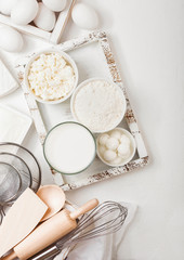 Fresh dairy products on white table background. Glass of milk, bowl of flour and cottage cheese and eggs. Box of baking utensils. whisk and spatula in vintage wooden box.Top view.