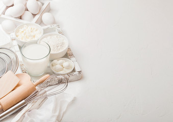 Fresh dairy products on white table background. Glass of milk, bowl of flour and cottage cheese and eggs. Box of baking utensils. whisk and spatula in vintage wooden box.Top view. Space for text