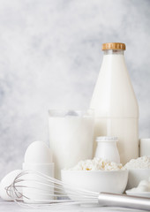 Fresh dairy products on white table background. Plastic bottle and glass of milk, bowl of cottage cheese and baking flour and mozzarella. Eggs and cheese. Steel whisk.