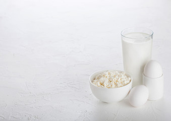 Fresh dairy products on white table background. Glass of milk, bowl cottage cheese and eggs. Space for text
