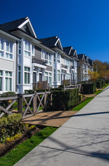 Row of new townhomes in a sidewalk neighborhood. On a sunny day in spring against bright blue sky.