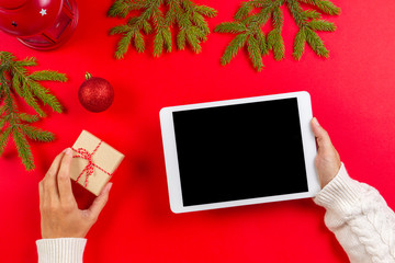 Top view of tablet computer in woman hands. Christmas decoration and fir branches on red background