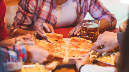 Close-up of real Italian pizza on table and  group of young college friends sitting around and picking up a slice. Best friends having fun together at party with pizza.
