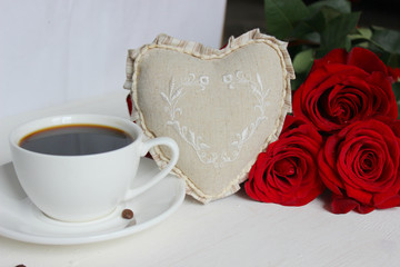 A Cup of coffee, a bouquet of red roses and a gift with a red ribbon on the table close-up. Valentine's day, birthday concept.
