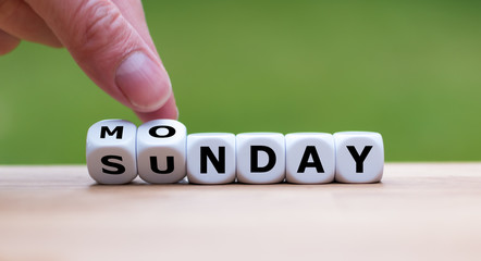 Hand is turning dice and changes the word Sunday to Monday