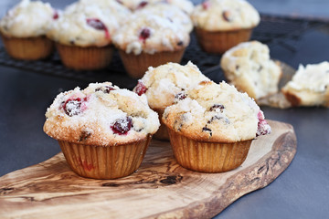 Cranberry Muffins with lemon sugar topping on a rustic cutting board with loose berries. Extreme shallow depth of field with blurred background.