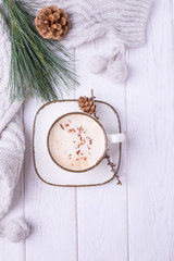 Fototapeta na wymiar Coffee cappuccino with ceylon cinnamon, a branch of a pine tree and knitted accessories on a white wooden background