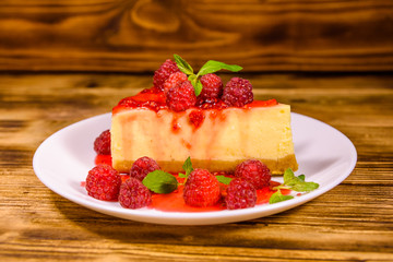 White plate with cheesecake New York, leaves of mint and raspberries on wooden table