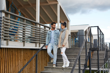 Positive young couple in autumn clothing holding hands and moving down stairs of cottage while chatting outdoors