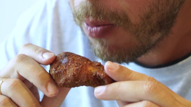 Closeup view of hungry bearded man eating tasty crispy chicken wings with great appetite at fast food restaurant. Real time full hd video footage.