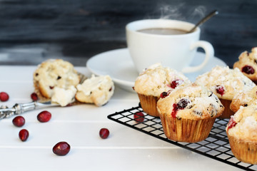 Cranberry Muffins cooling on a bakers rack with extreme shallow depth of field and open muffin with butter and a steaming hot cup of coffee in the background. Selective focus on muffin in the center.