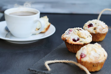 Cranberry Muffins on a slate serving tray with open muffin with butter and a steaming hot cup of coffee in the background. Extreme shallow depth of field with selective focus on center muffin.