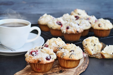 Cranberry Muffins on a wood cutting board with more cooling on a bakers rack. Extreme shallow depth of field with selective focus on muffin in foreground. Steaming hot cup of coffee in the background.