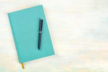 A photo of a teal blue journal with a pen, an elegant diary, notebook or planner, shot from above...