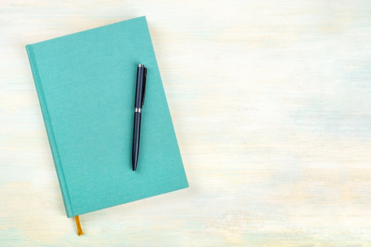 A photo of a teal blue journal with a pen, an elegant diary, notebook or planner, shot from above with copy space