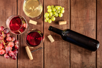 Wine Tasting in a Cellar. A photo of glasses of red, rose, and white wine with a bottle, grapes, and a vintage corkscew and corks, shot from the top on a dark rustic wooden background with copy space