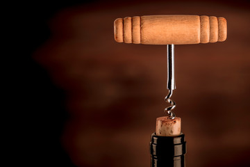A closeup photo of a vintage corkscrew in a bottle of wine, on a dark background with copy space. Toned image