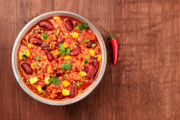 A photo of chili con carne, traditional Mexican dish, with a chilli pepper, shot from the top on a dark rustic wooden background with a place for text