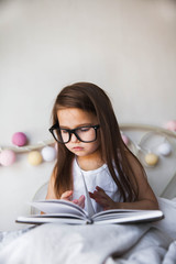 Beautiful girl reading a book in bed wearing glasses, education, interests, prospective student