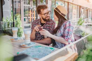 Lovely couple sit together and look at each other. She holds phone in hands. He point on it. They...