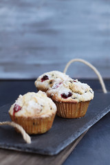 Cranberry Muffins with lemon sugar topping on a rustic slate serving tray. Extreme shallow depth of field with selective focus on muffin in center.