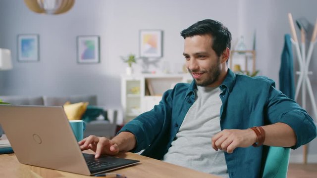 Portrait of Handsome Relaxed Man Using Laptop while Sitting at His Desk at Home. Guy Watching Movies, Videos or Browsing Internet.
