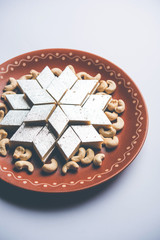 Kaju Katli is a Diamond shape Indian sweet made using cashew sugar and mava, served in a plate or bowl over moody background. selective focus