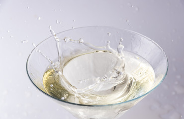 A glass with vermouth and a piece of ice thrown at it. splash and splash of drink