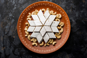 Kaju Katli is a Diamond shape Indian sweet made using cashew sugar and mava, served in a plate or bowl over moody background. selective focus