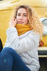 Portrait of young attractive redhead curly girl siting front of yellow van and smiling