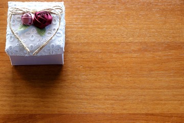 Gift box on wooden background. White box with flowers and ribbon in shape of heart.