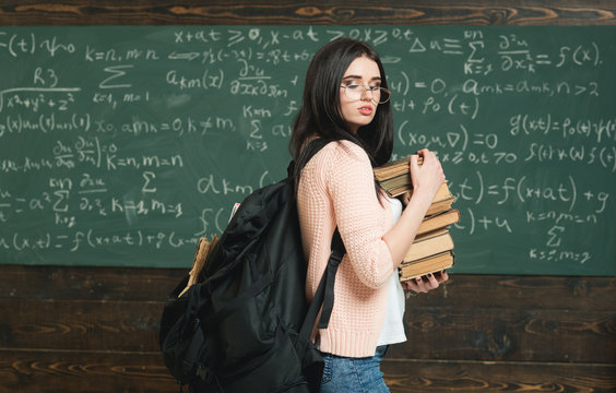 Girl with big backpack holds pile books, chalkboard background. Girl student works on research. Diligent student preparing for exam test. Baggage of knowledge. Student excellent accumulates knowledge