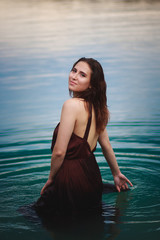 Fototapeta na wymiar Beautiful young girl by the lake. Girl in a dress on the beach
