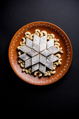 Kaju Katli is a Diamond shape Indian sweet made using cashew sugar and mava, served in a plate or bowl over moody background. selective focus