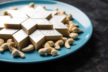 Kaju Katli is a Diamond shape Indian sweet made using cashew sugar and mava, served in a plate or bowl over moody background. selective focus