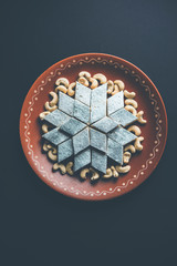 Kaju Katli is a Diamond shape Indian sweet made using cashew sugar and mava, served in a plate or bowl over moody background. selective focus