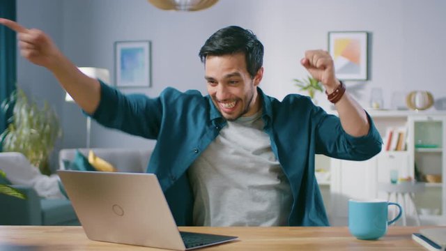 Happy Handsome Man Working on a Laptop Celebrates Successful Endeavor with YES Gesture. Freelances Working from His Living Room Has Stroke of Luck and Wins Big.