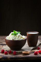 Cottage cheese and milk in clayware on wooden table, sackcloth table-napkin and wooden spoon
