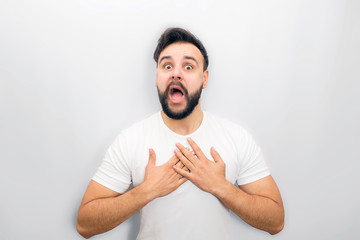 Scared and frightened young man looks on camera with mouth opened. He keeps hands close on chest. Guy is surprised. Isolated on white background.