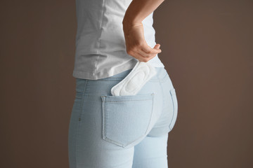 Woman putting menstrual pad into pocket on color background