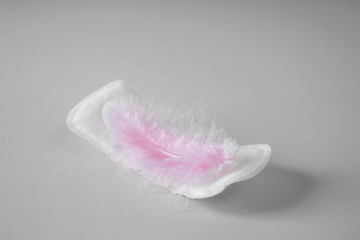 Menstrual pad with feather on grey background