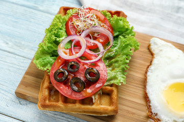 Delicious waffle with vegetables and fried egg on wooden board