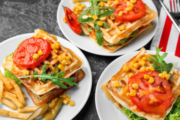 Delicious waffles with french fries and vegetables on plates