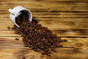 Roasted coffee beans spill out of cup on wooden table