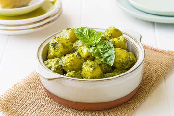 Gnocchi with 'Pesto' sauce, in terracatta bowl, on white woodwn background.