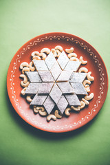 Kaju Katli is a Diamond shape Indian sweet made using cashew sugar and mava, served in a plate or bowl over moody background. selective focus