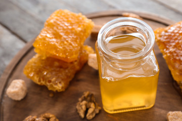 Full jar of honey and honeycomb on wooden board, closeup
