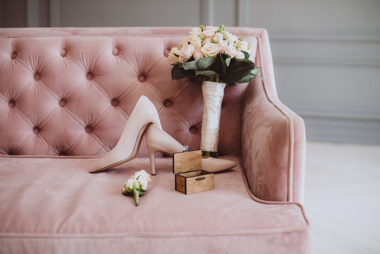 Bridal bouquet with wedding shoes and wedding rings on a vintage sofa