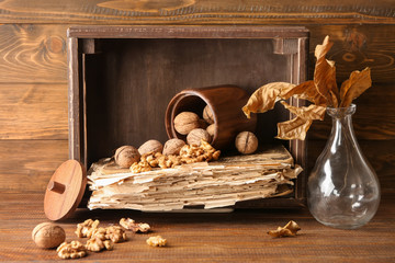 Composition with walnuts, old book and vase with dry leaves on wooden table